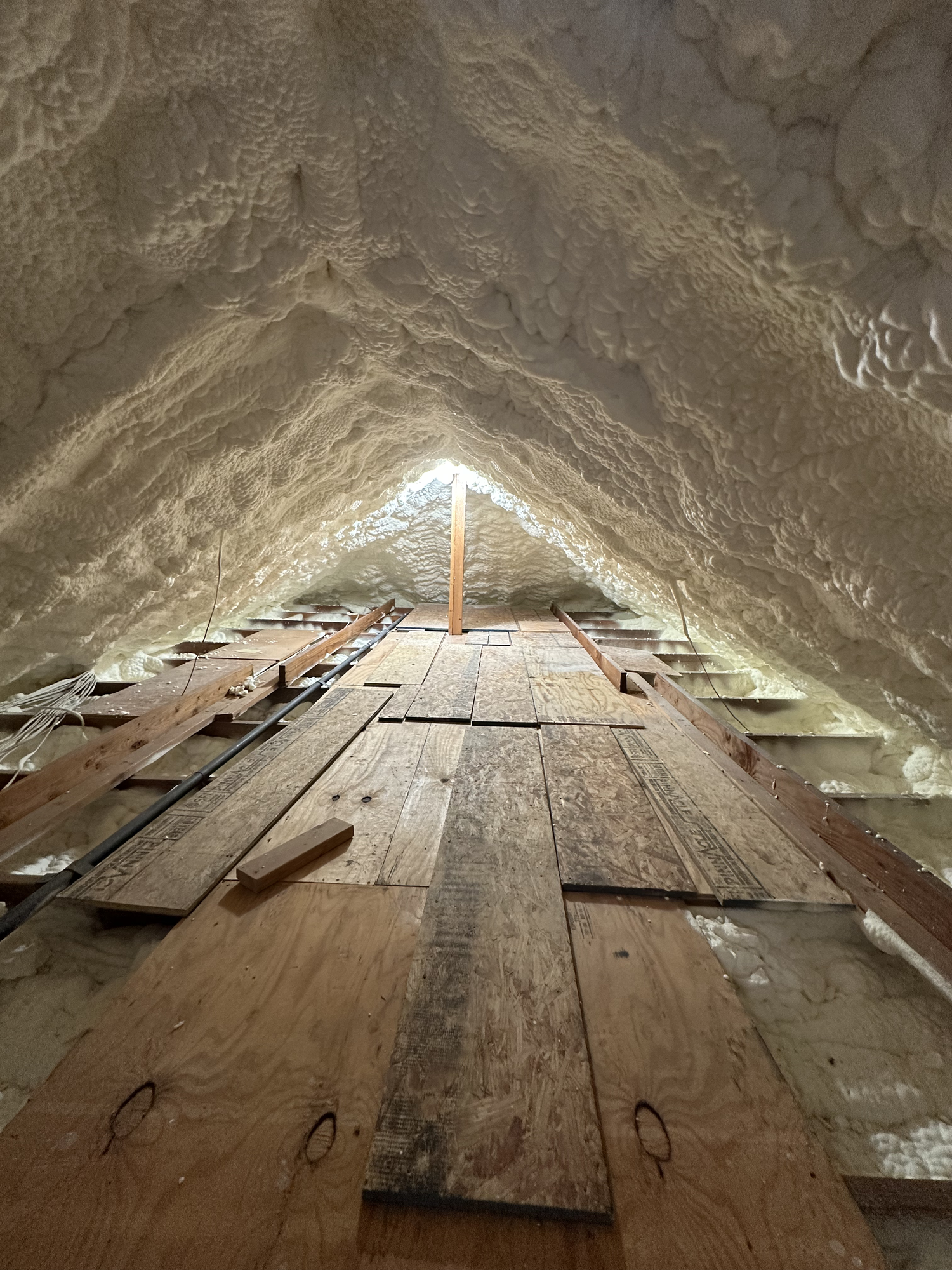 Attic with spray foam insulation on the roof deck and a plank walkway